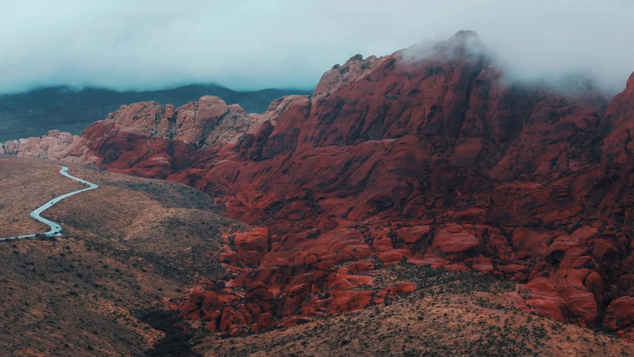 Red sandstone mountains with a winding road disappearing into low clouds.