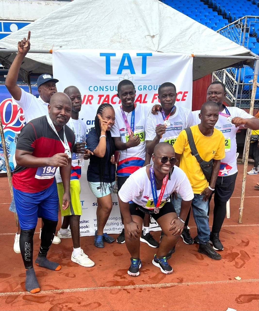 TAT group smiling together with race numbers and medals in front of a TAT banner.