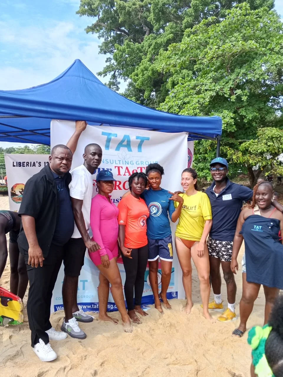 TAT group and other participants at a beach event beside a TAT banner.