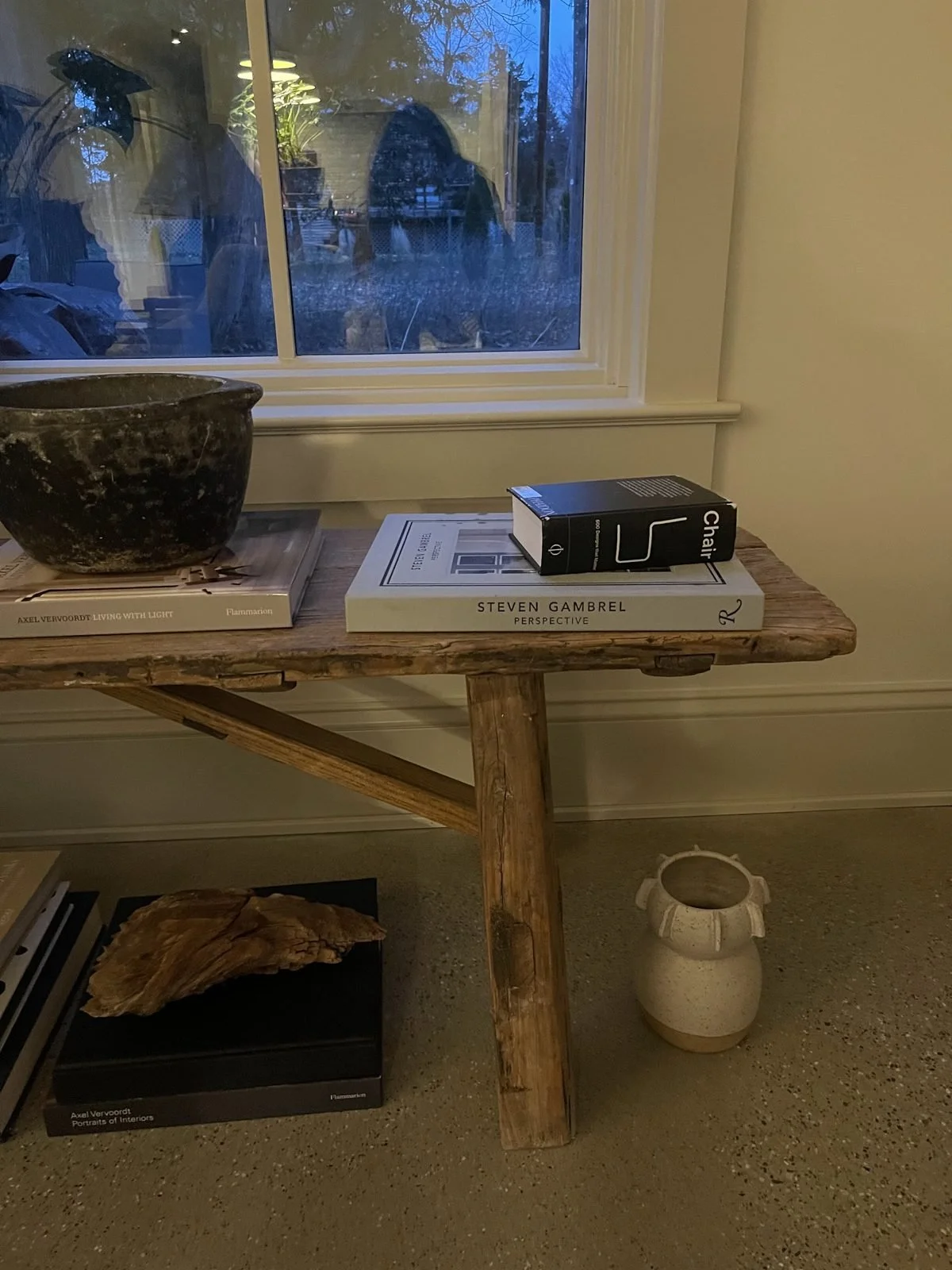 A rustic wood console beneath a window with books and a pottery bowl
