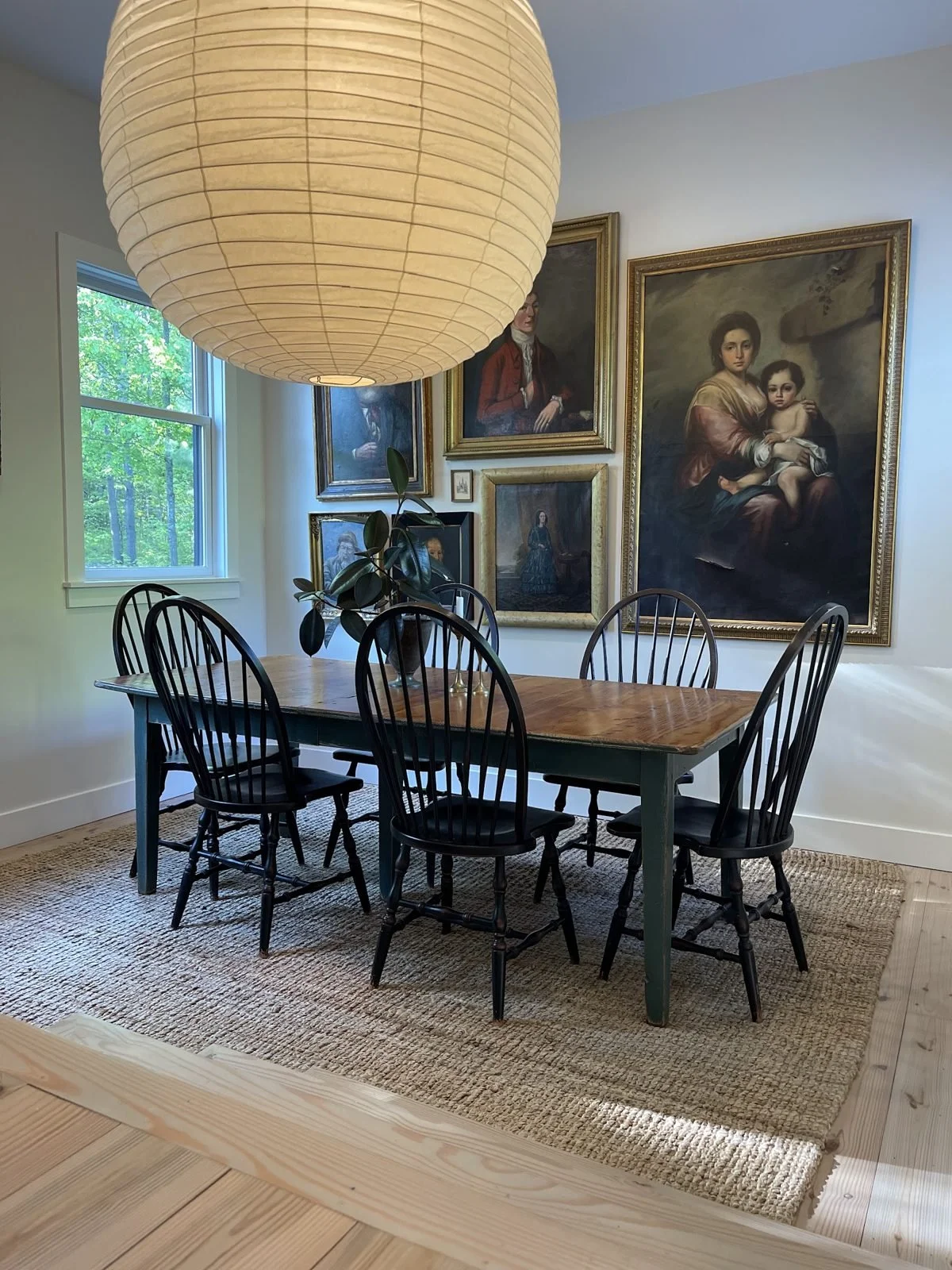 A dining room with black Windsor chairs, a paper lantern and old portraits