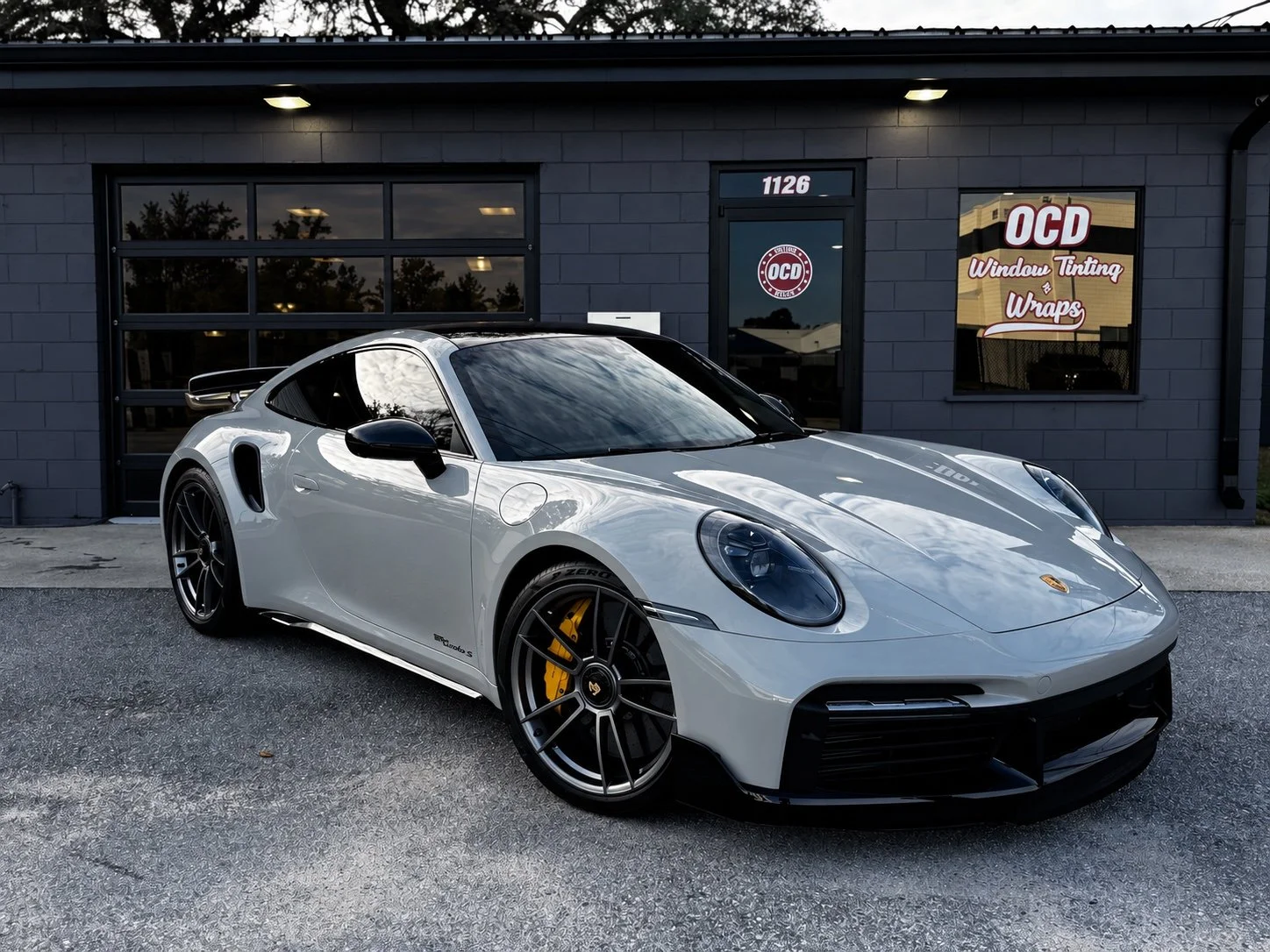 Grey Porsche Turbo S outside OCD Tinting & Wraps with a black glass garage door.