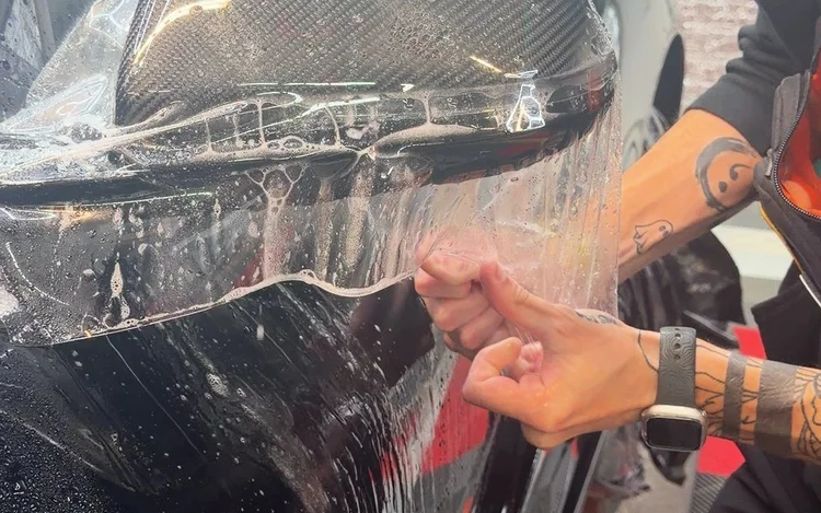 Installer stretching clear paint protection film over a vehicle panel.