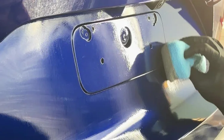 Gloved technician applying a ceramic coating to blue paint.