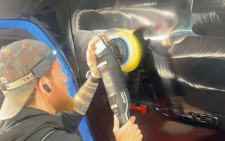 Machine polisher with a yellow pad correcting black paint.
