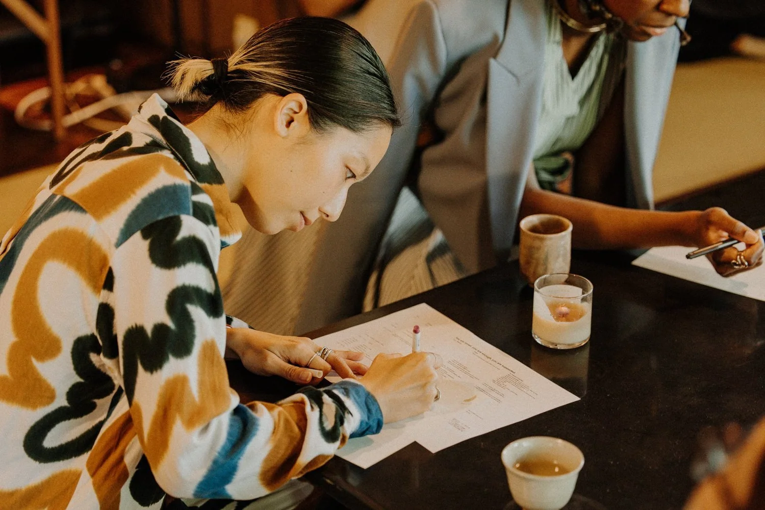 A participant writing on a reflection worksheet beside cups of tea and a candle
