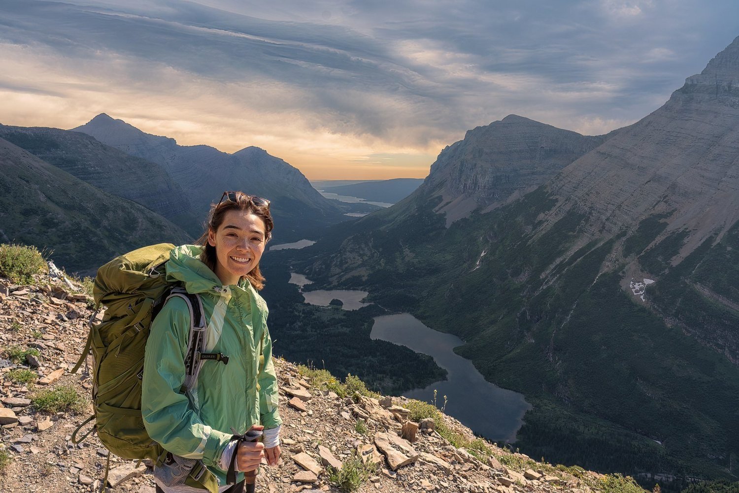 Nina smiling with a hiking pack above a valley of lakes in the mountains of Montana