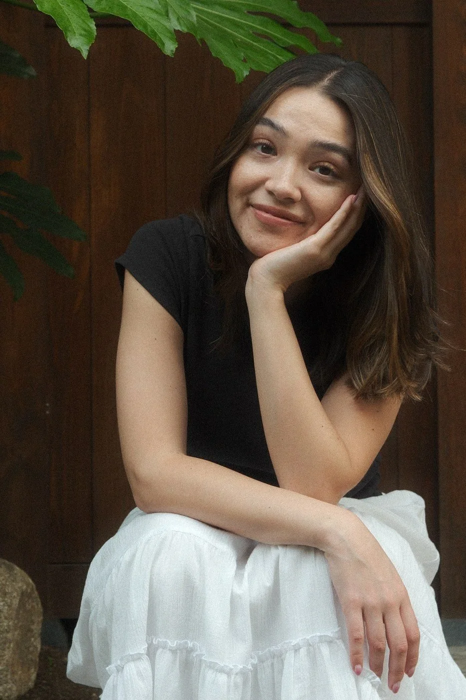 Nina sitting outside a wooden doorway, chin resting on her hand, smiling