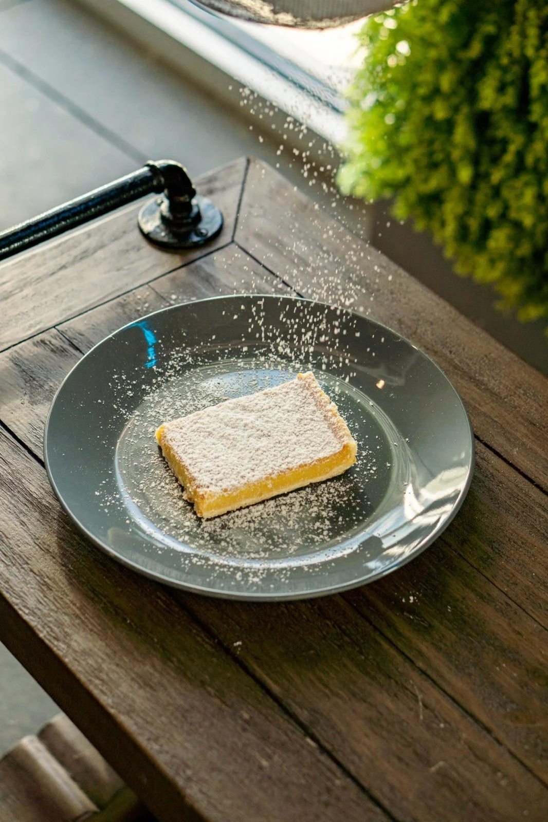 A square yellow dessert on a plate beside a window