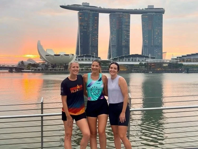 Three Pretty Strong athletes at the Marina Bay waterfront as the sun comes up behind Marina Bay Sands