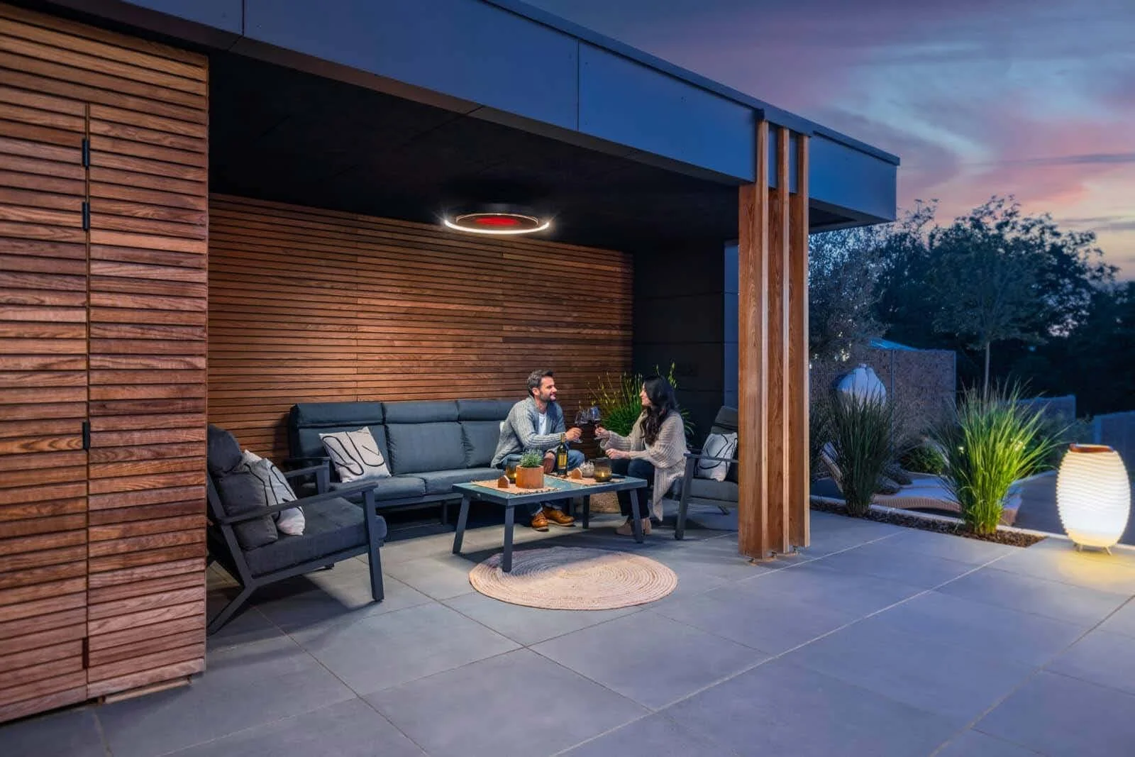 A Bromic Eclipse pendant heater lights a covered outdoor lounge at dusk