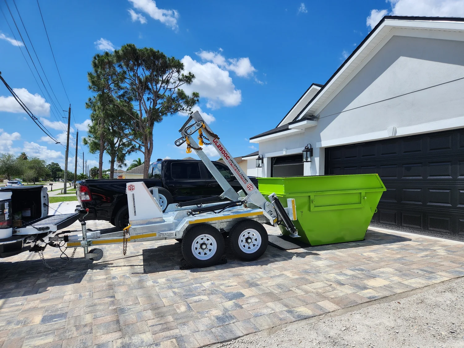 A green DropSkip mini dumpster being placed on a residential paver driveway beside a garage in Brevard County, FL