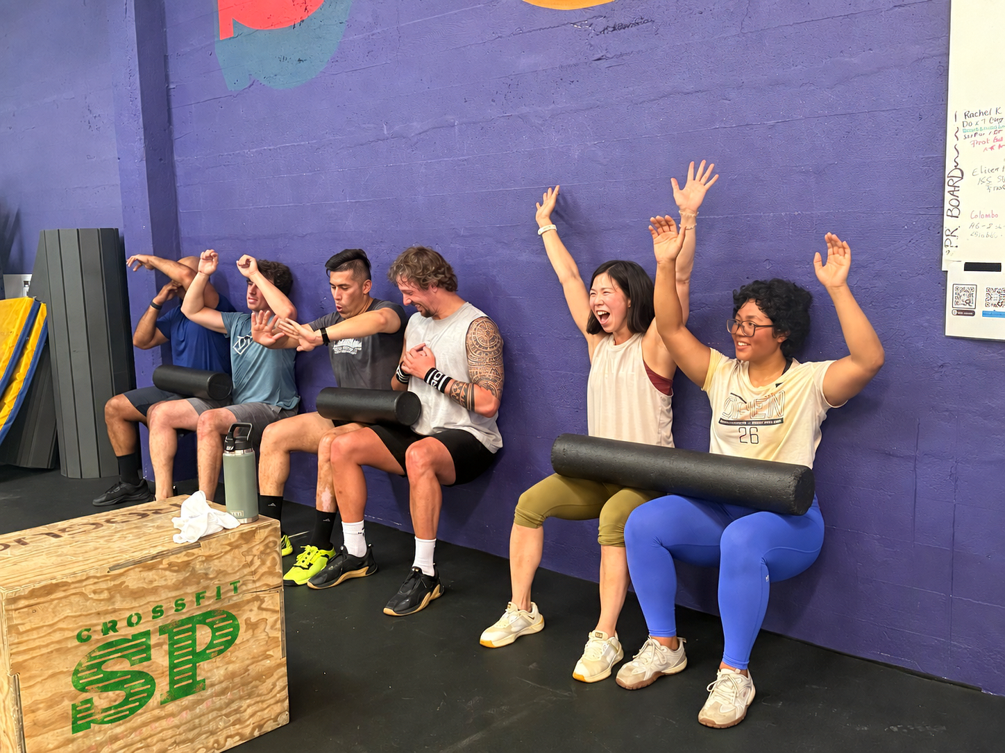 CrossFit South Park athletes laughing together during a partner foam roller wall sit