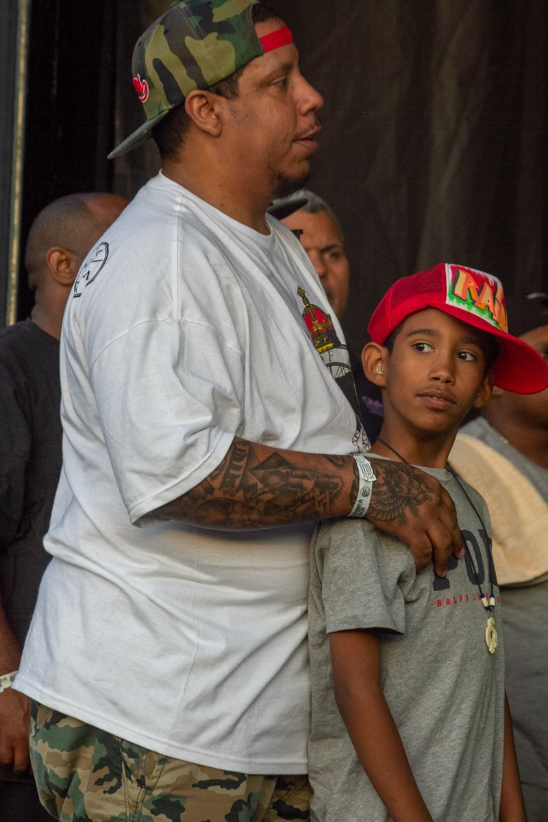 Pumpkinhead stands with his son Raiden onstage as they watch Rakim perform during an outdoor hip-hop concert.