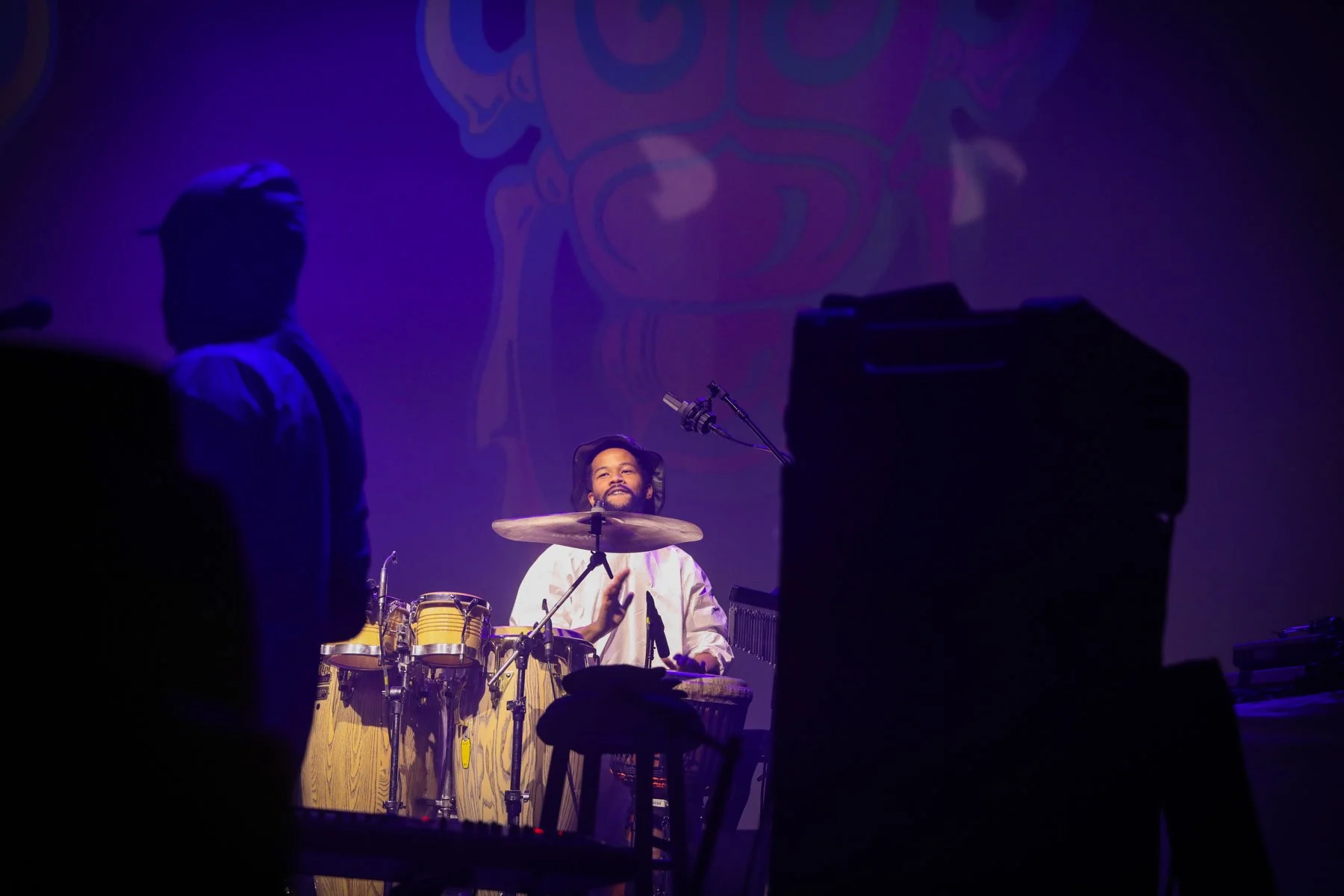 Percussionist performing behind congas and drums under purple stage lighting