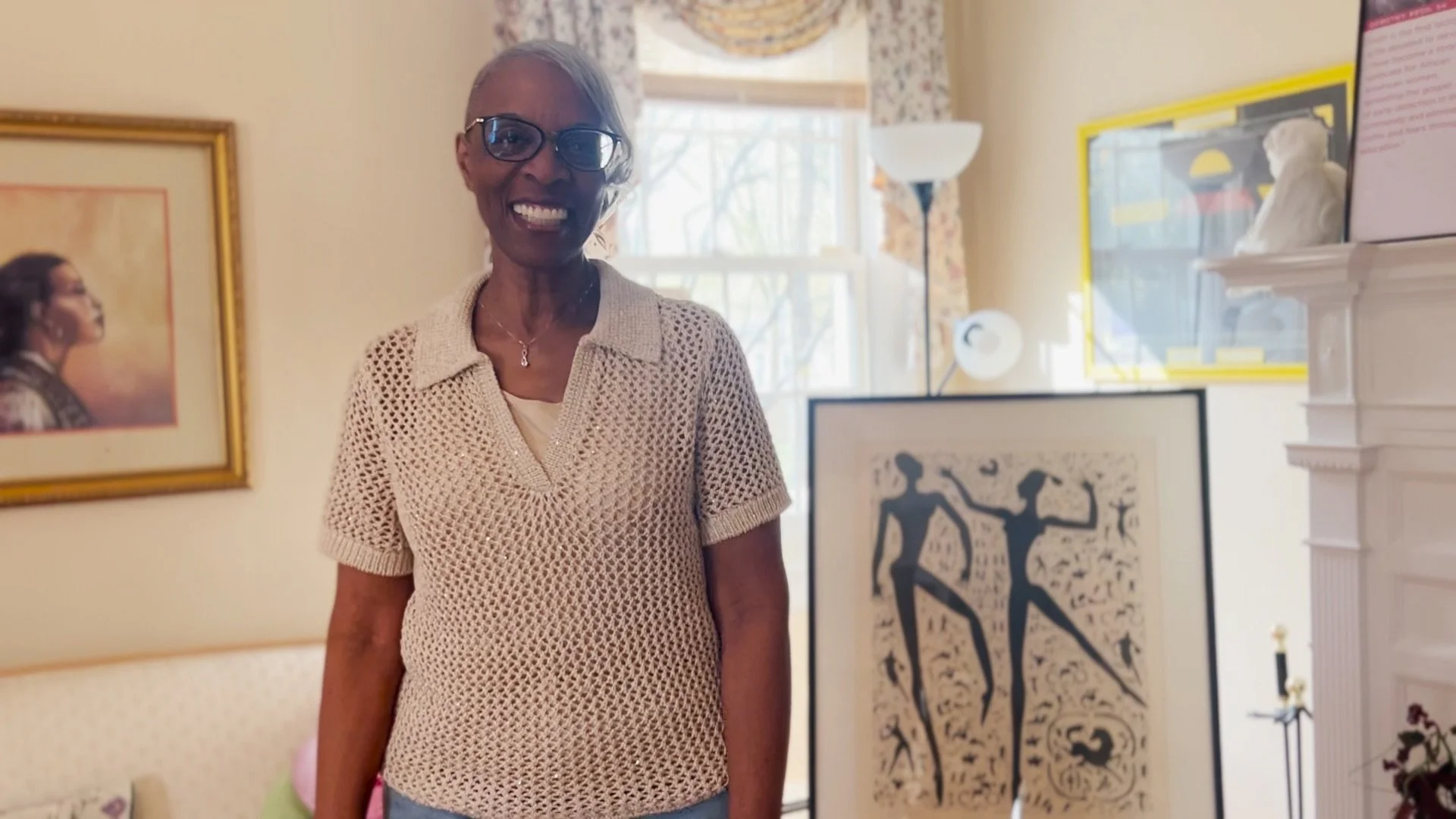 Dorothy J. Reed smiling inside the Sister2Sister Somerset facility while gesturing toward a framed portrait of Pearl Grace