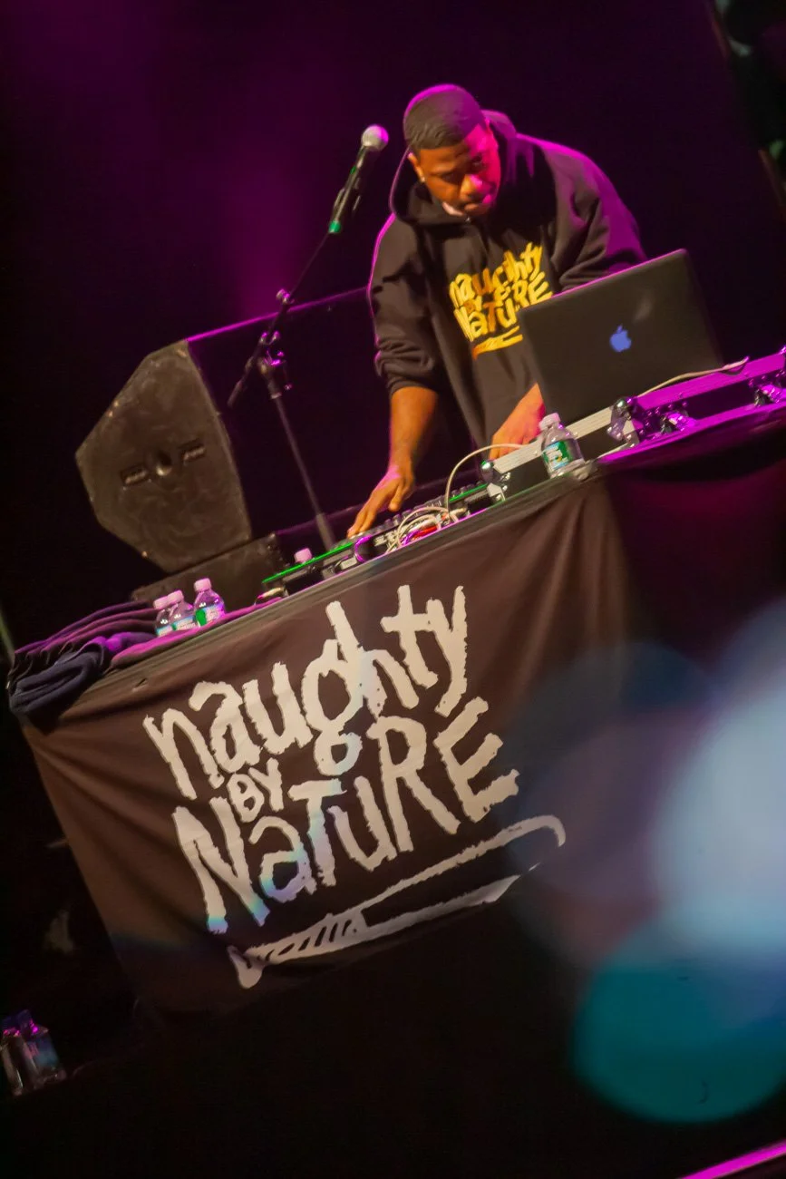 DJ performing behind equipment with a Naughty by Nature banner