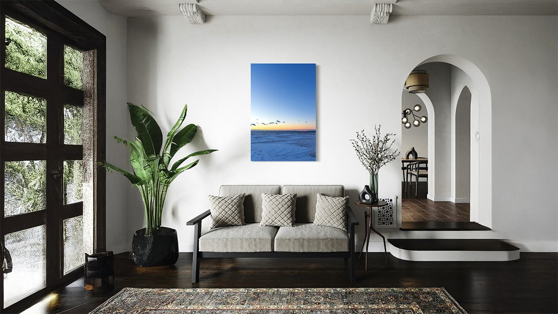 Framed twilight photograph with birds above a blue sea and an orange horizon, displayed in a living room