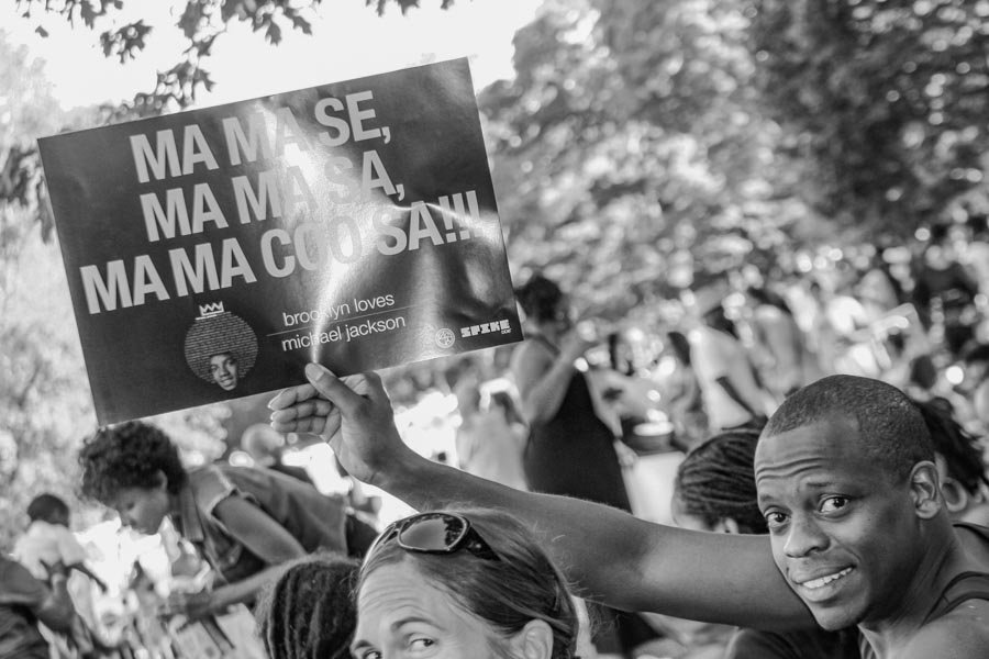 Young person holding a handwritten Mama Say Mama Sa tribute sign
