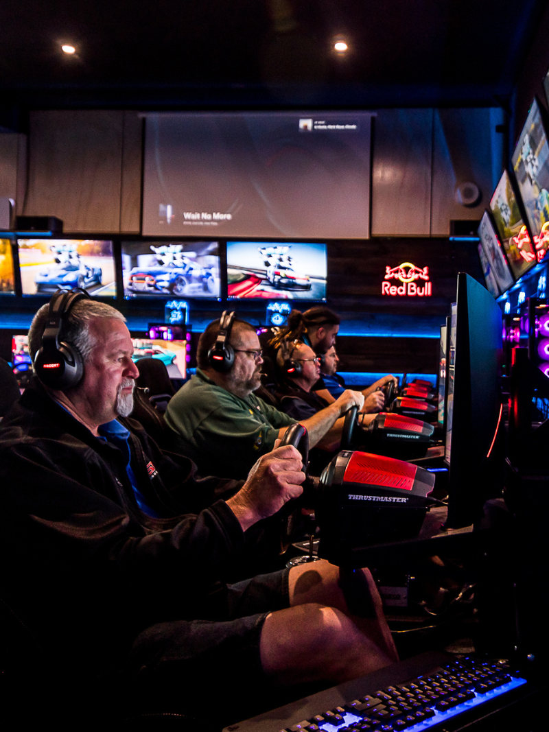 Sim racing rig with steering wheel and multiple monitors showing a racetrack