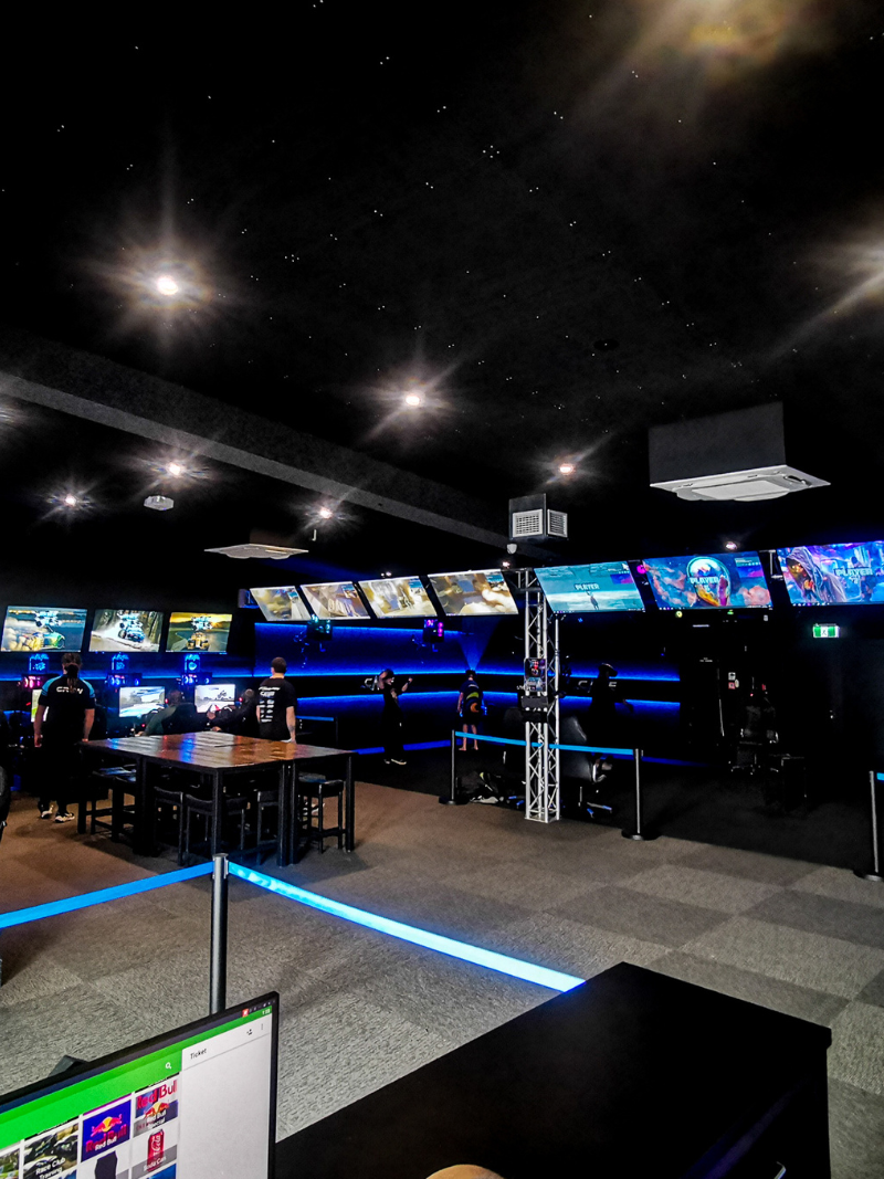Row of sim racing rigs with steering wheels and monitors showing a racetrack