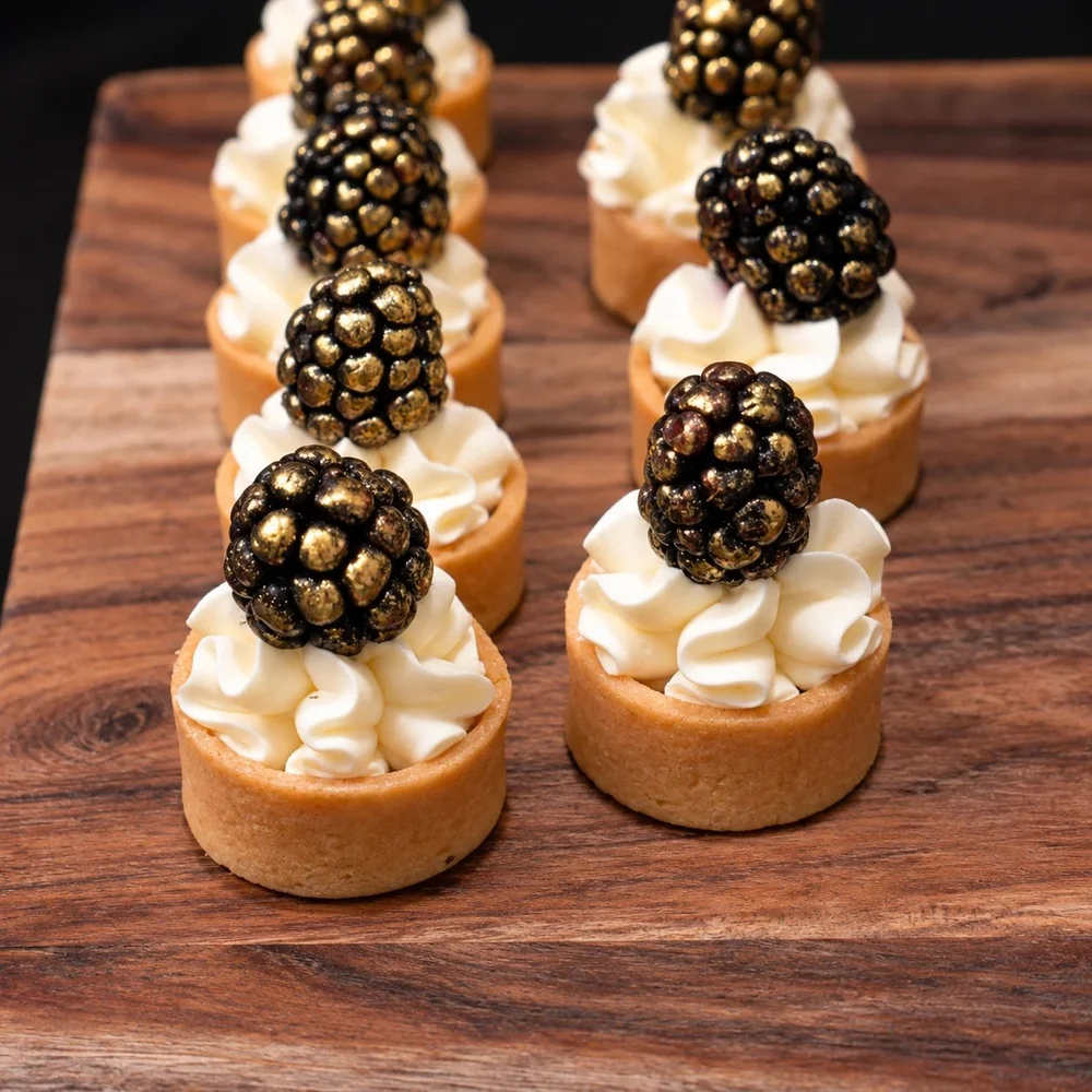 Mini cream tarts topped with gold-dusted blackberries