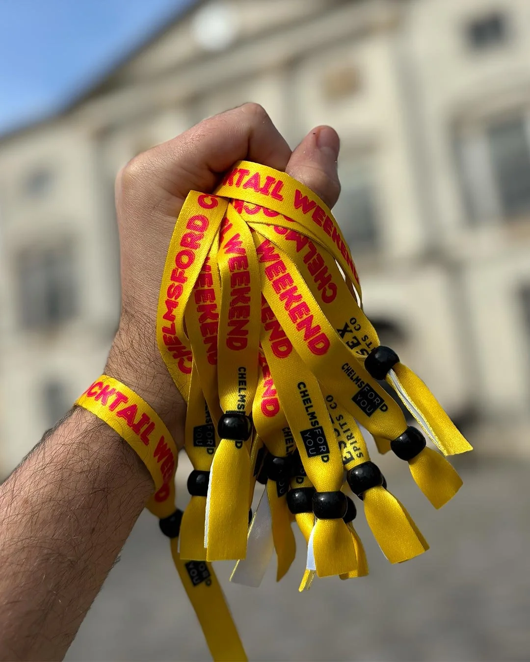 Yellow Chelmsford Cocktail Weekend wristbands held in a hand