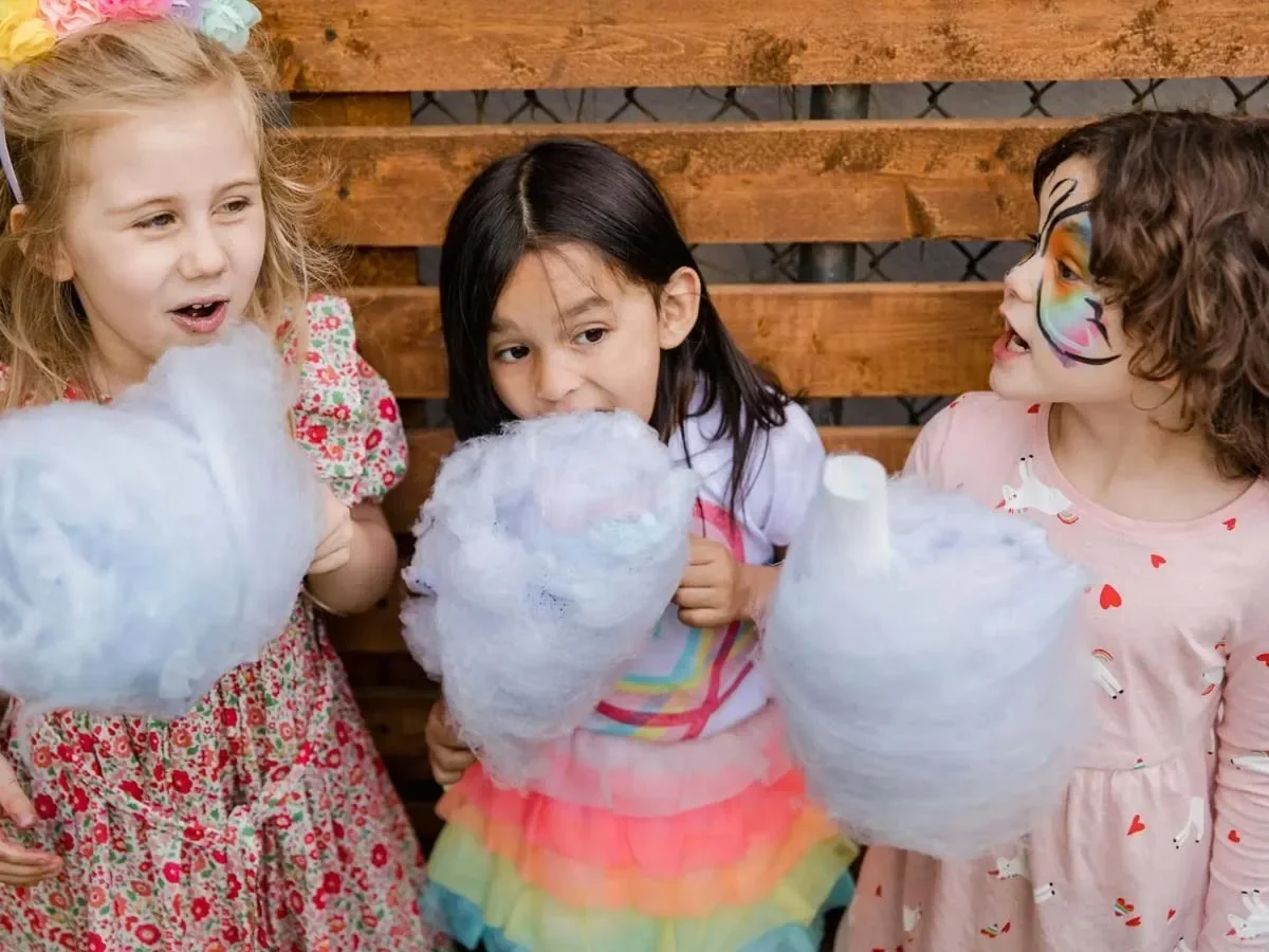 Three children holding candyfloss at a family event.
