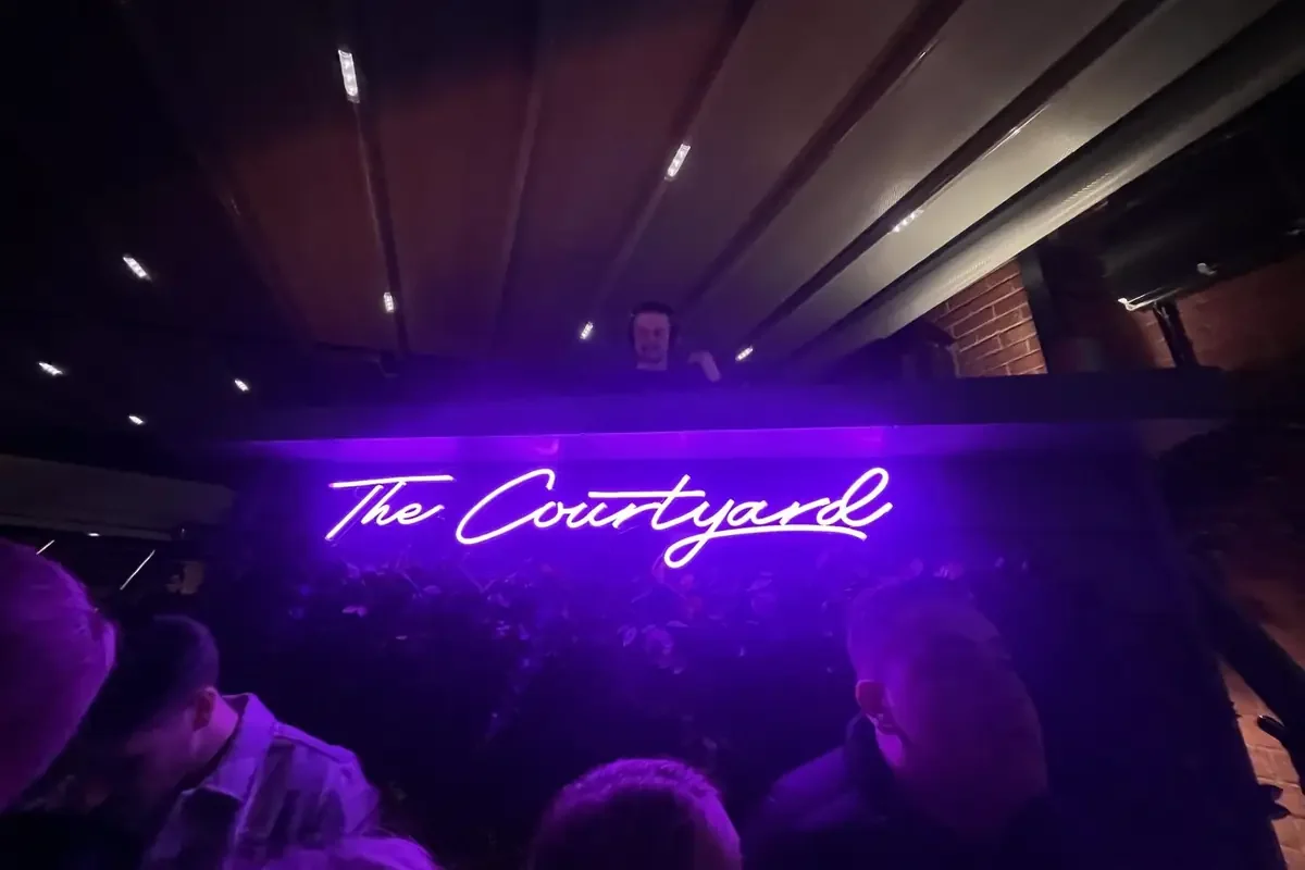 The Courtyard’s illuminated sign above a busy evening crowd.