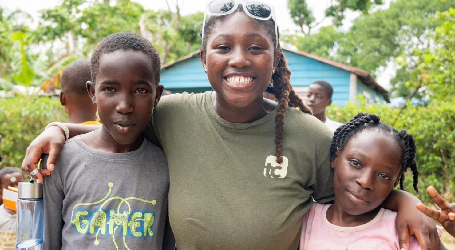 A smiling team member with her arms around two children on a mission trip