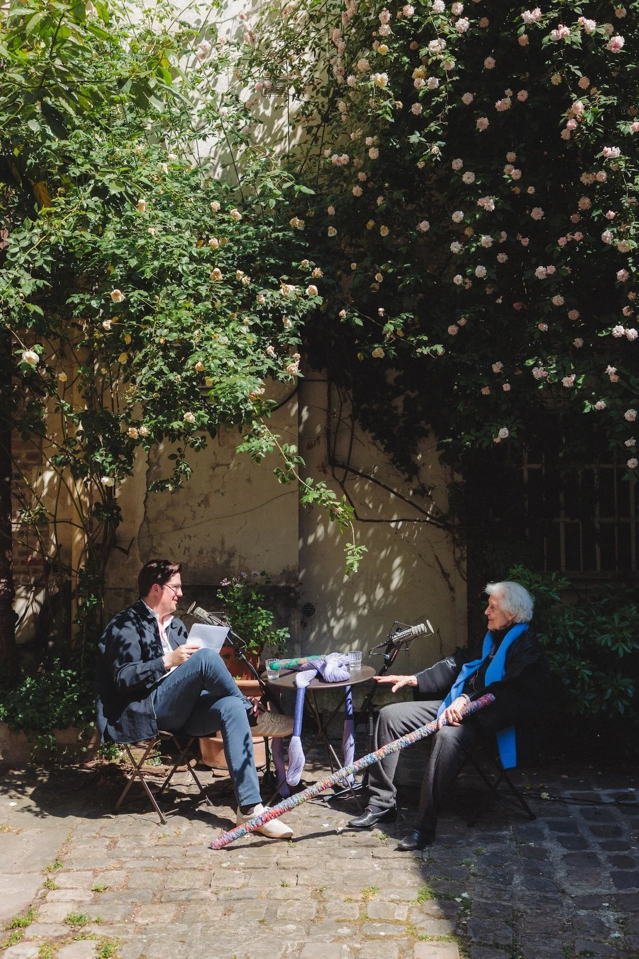 Spencer Bailey and Sheila Hicks seated with microphones and textile works in her Paris courtyard.