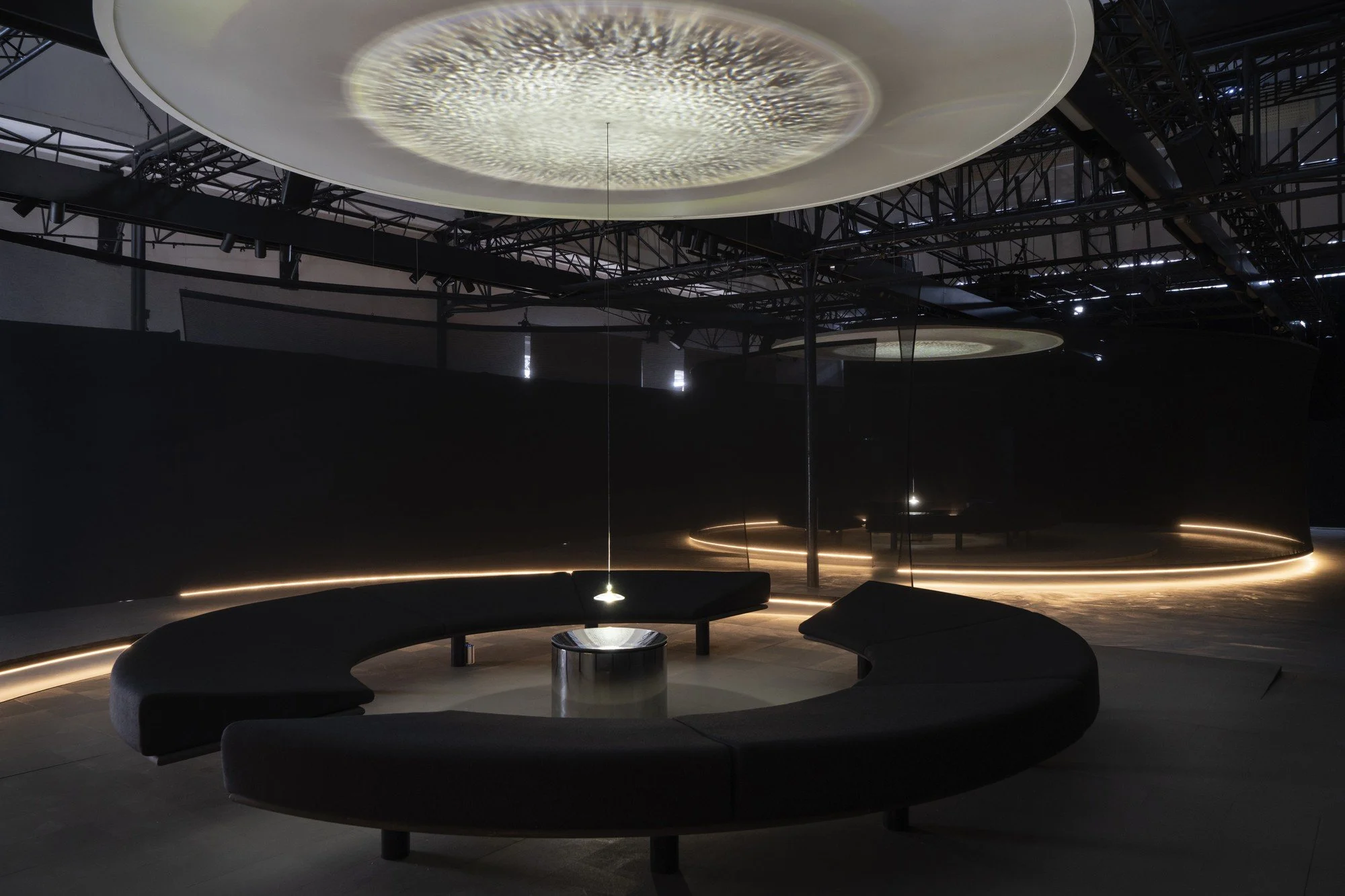 Water patterns projected onto a circular overhead surface above curved seating and a reflective vessel in Lachlan Turczan’s Wavespace installation for Google.