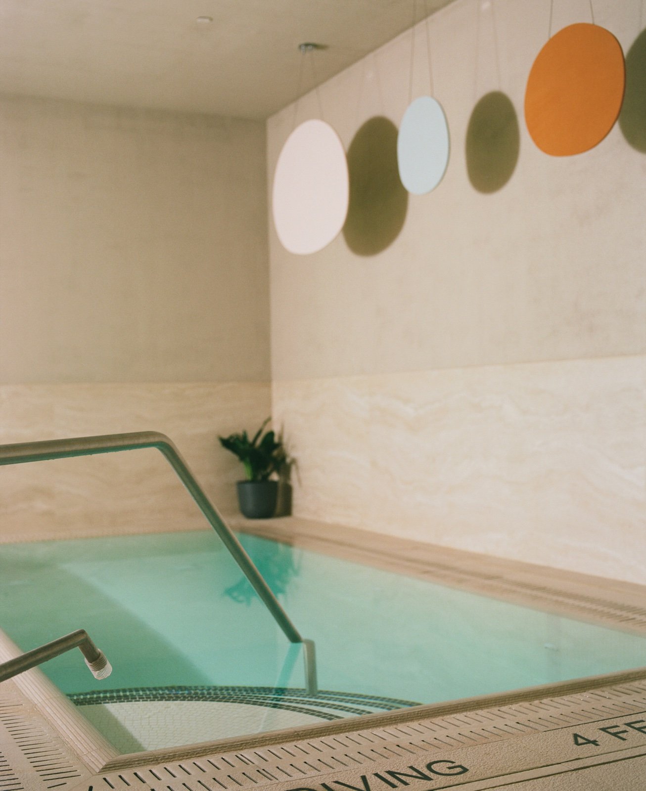 The cold plunge at Lore Bathing Club, with travertine walls, blue-green water and a hanging mobile.