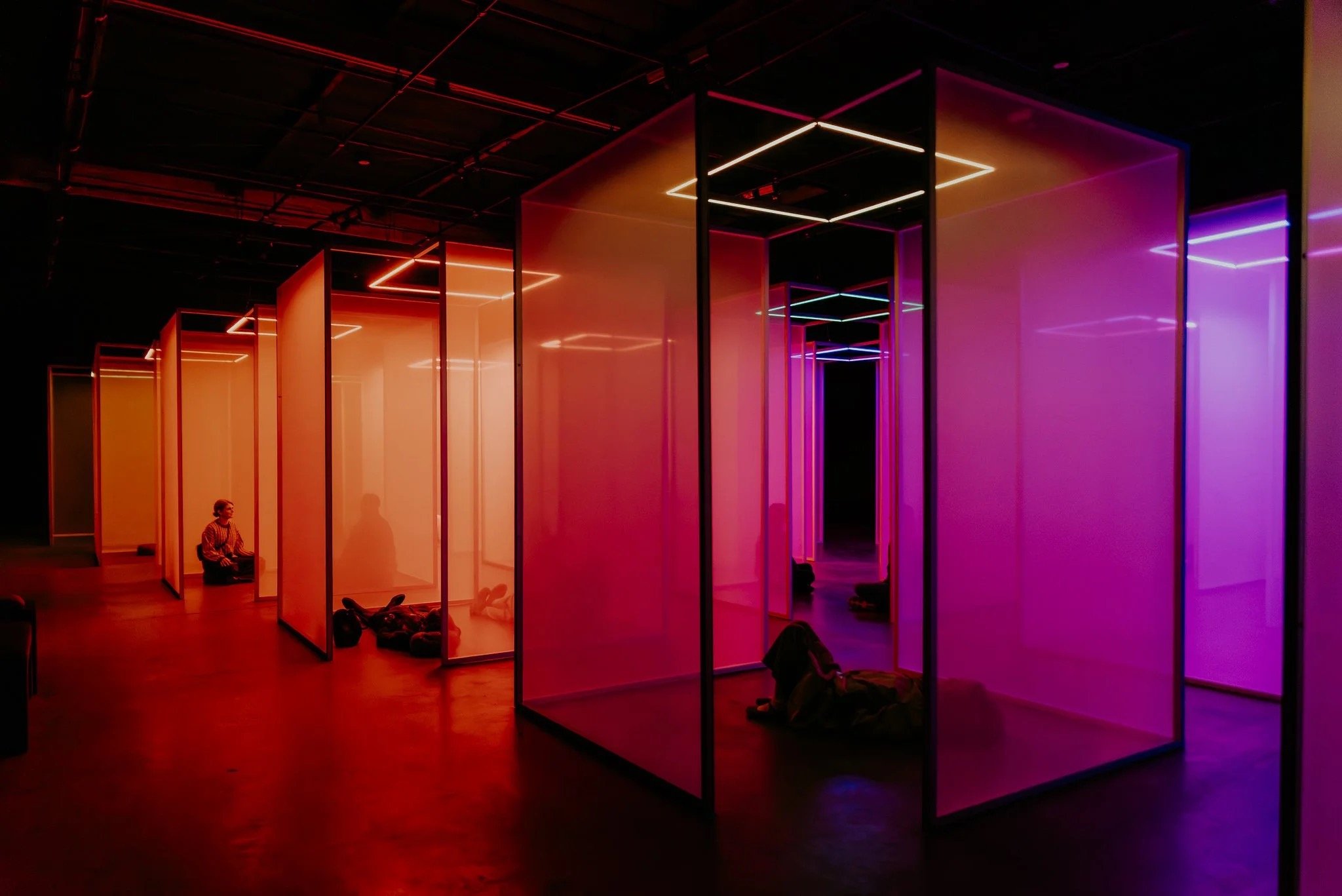 Visitors seated and reclining within orange and purple illuminated rooms at Chromasonic Field in Los Angeles.