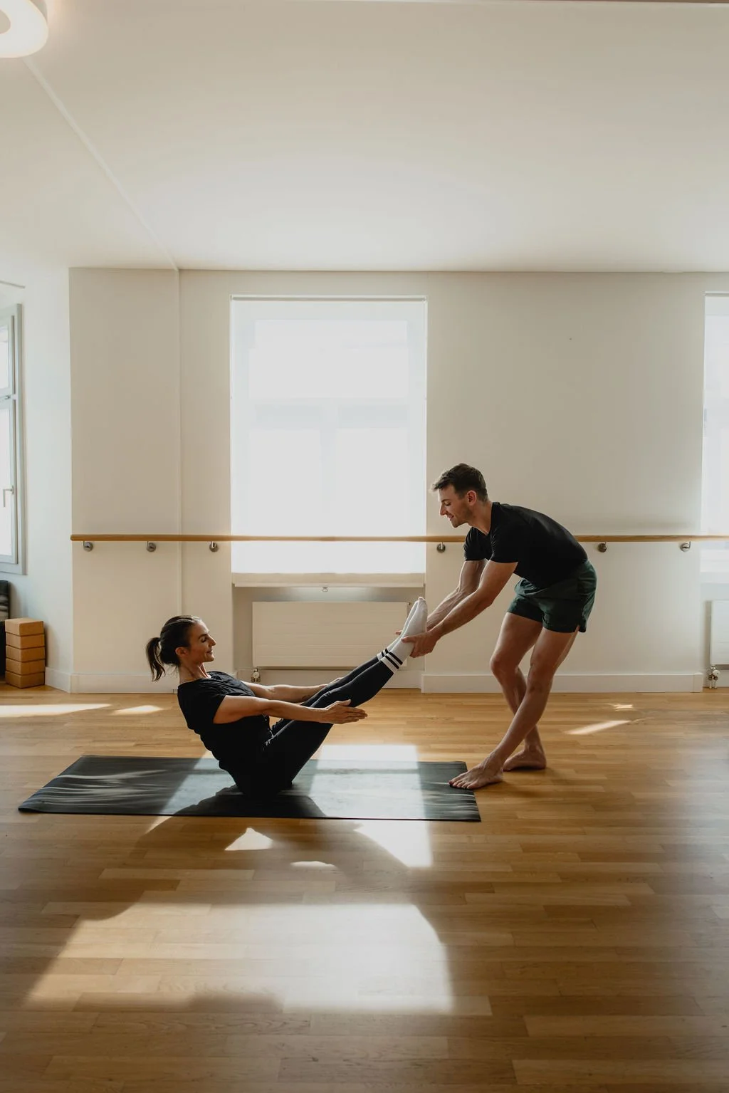 An instructor guiding a client through Mat Pilates in the sunlit studio