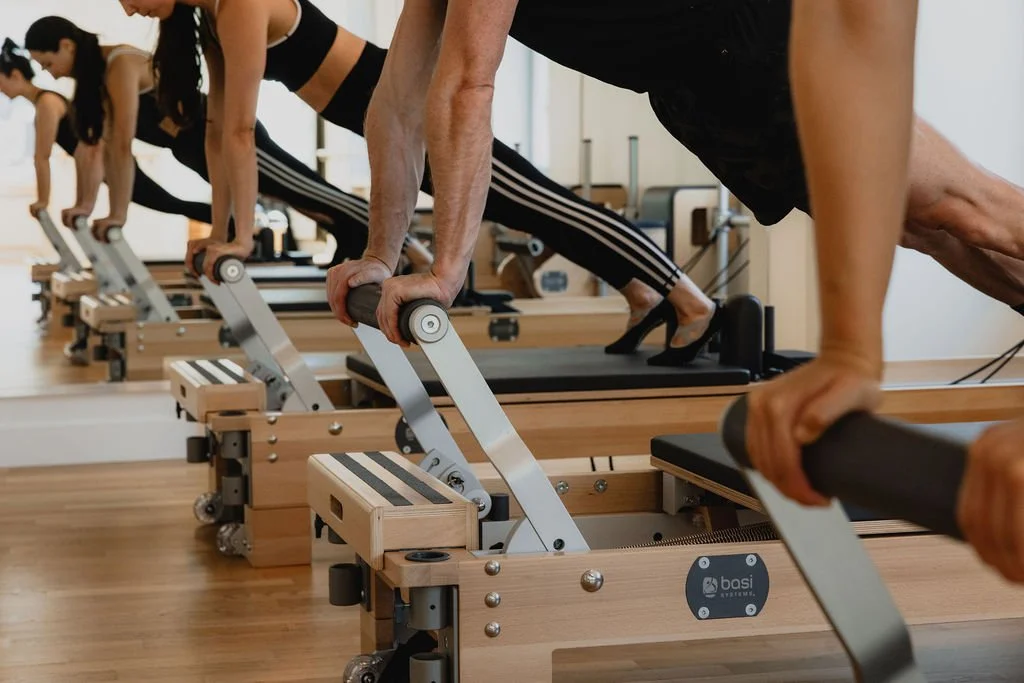 Hands supporting advanced Reformer practice on the footbar