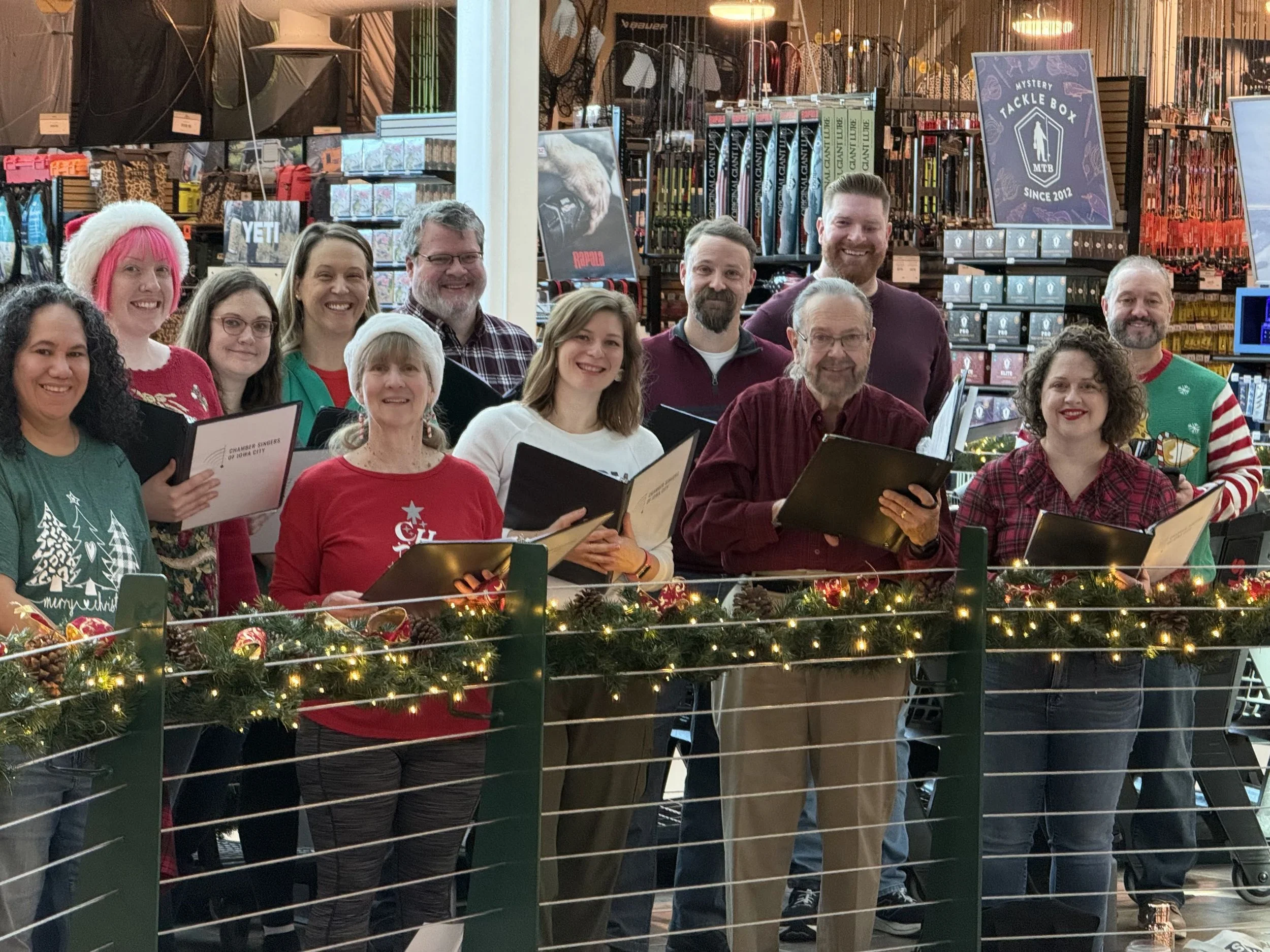 Chamber Singers caroling behind a lit garland at a local business