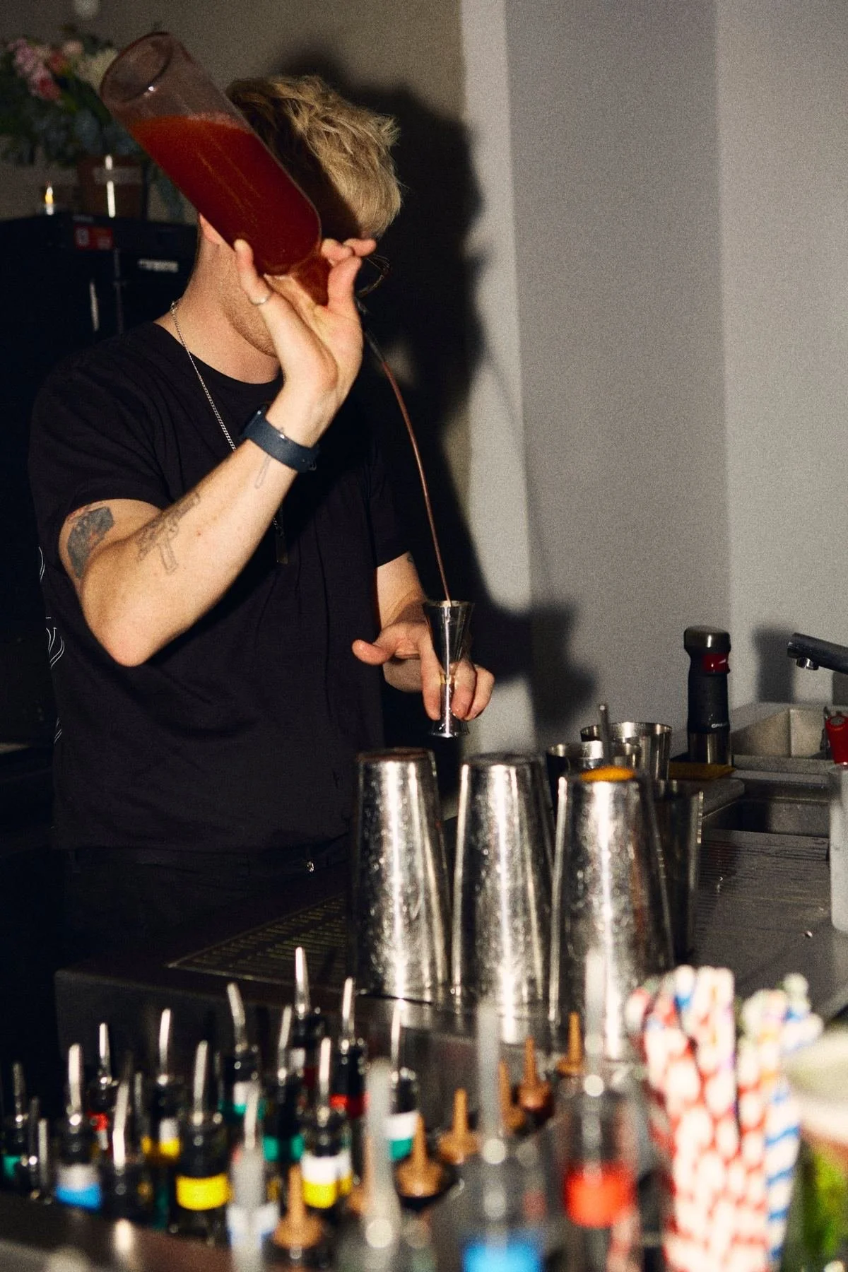 Un bartender abocant en un jigger sobre una fila de cocteleres.