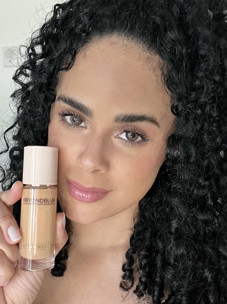 A creator with curly hair holding a bottle of BeyondBlur foundation