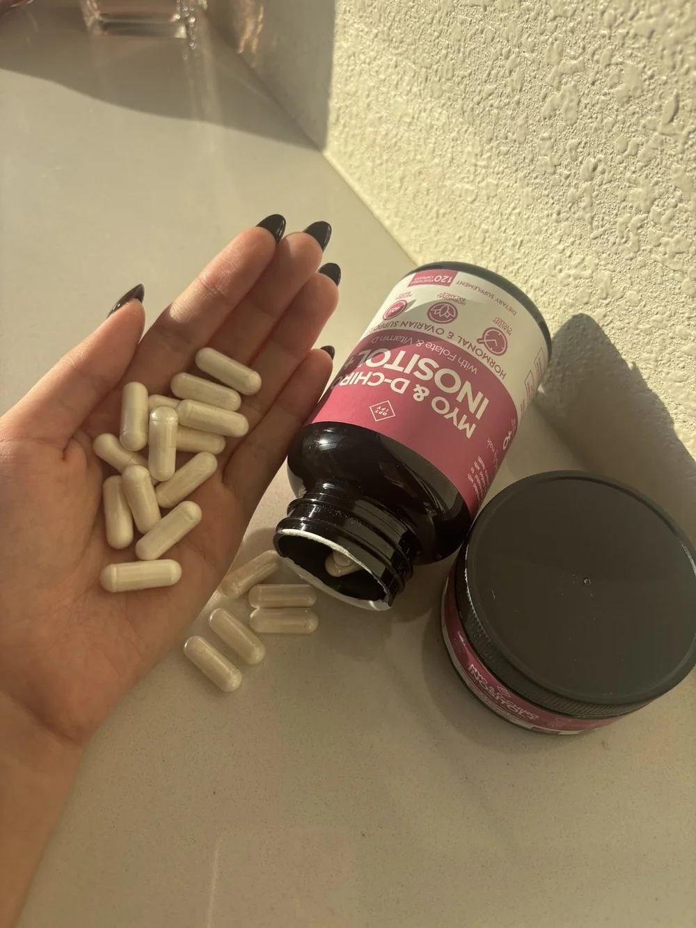 Inositol capsules in an open palm next to the bottle