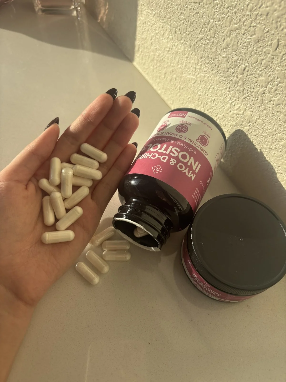 Inositol capsules in an open palm next to the bottle
