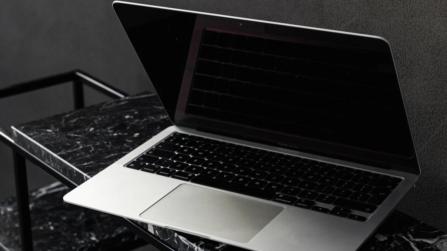 An open laptop on a black marble desk against a dark wall
