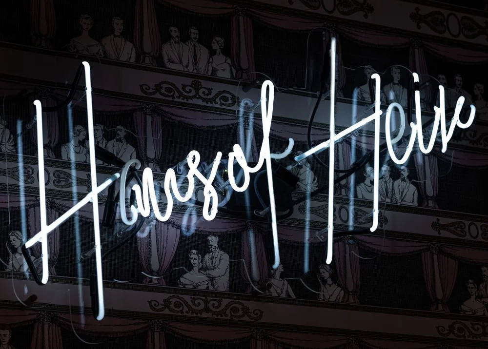 A white neon Haus of Heir script sign on a dark wall
