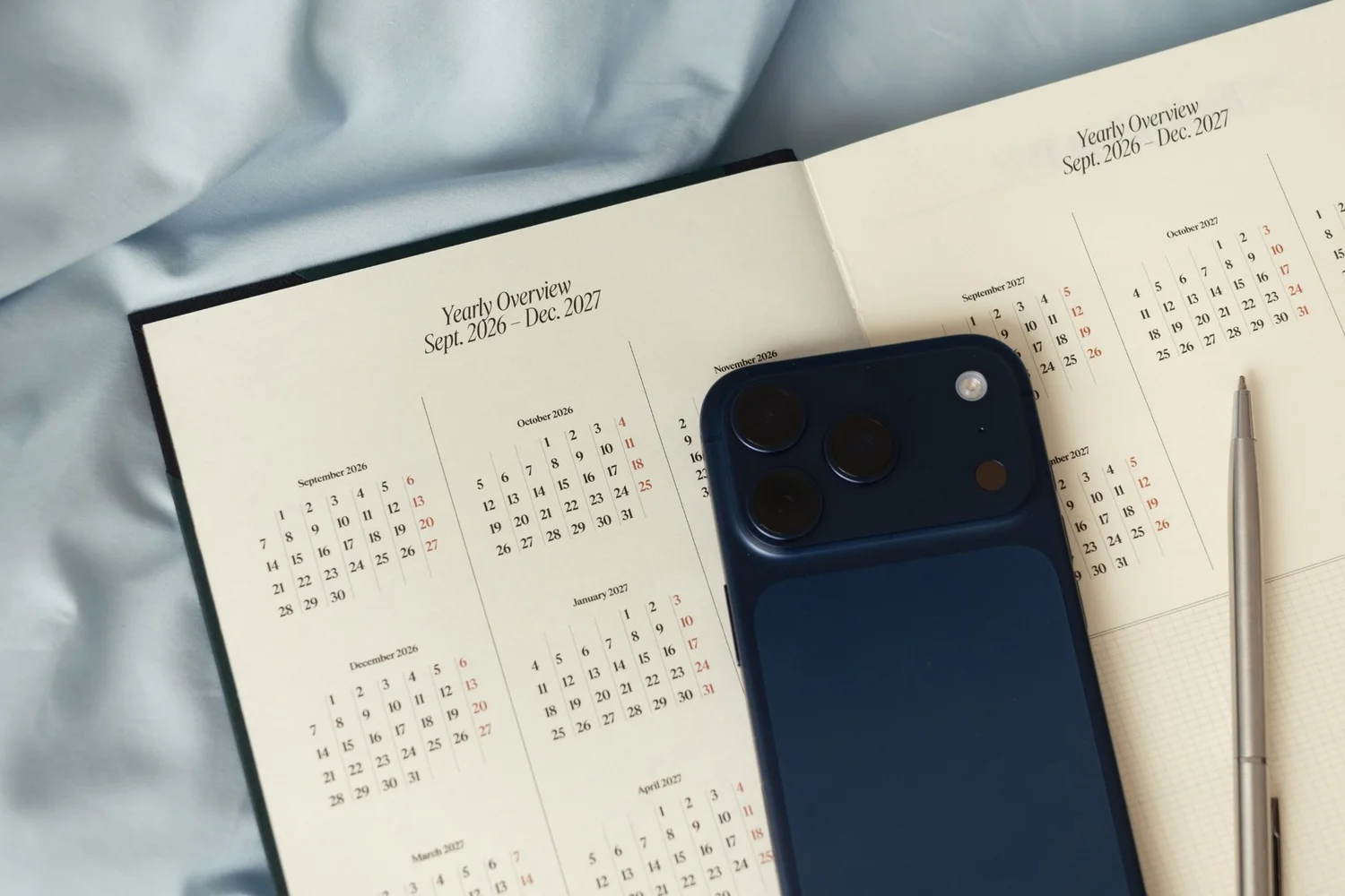 A navy phone and a silver pen on an open yearly planner