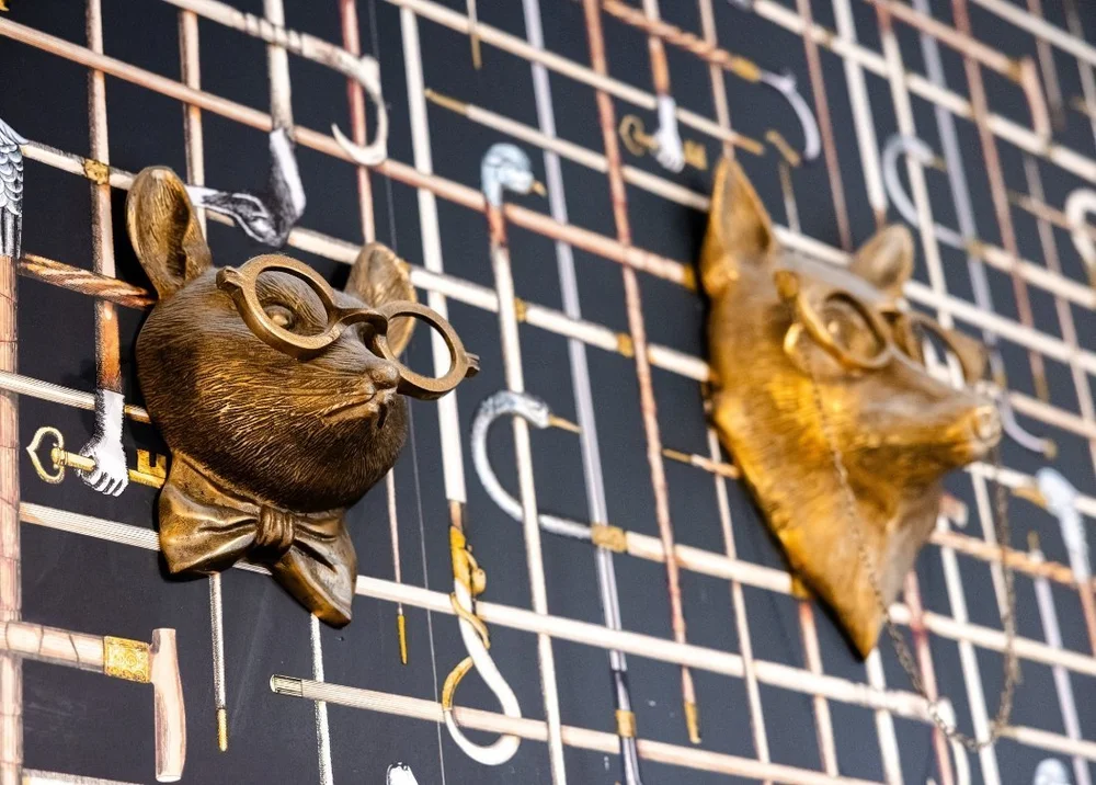 Gold animal heads with glasses mounted on a black grid wall