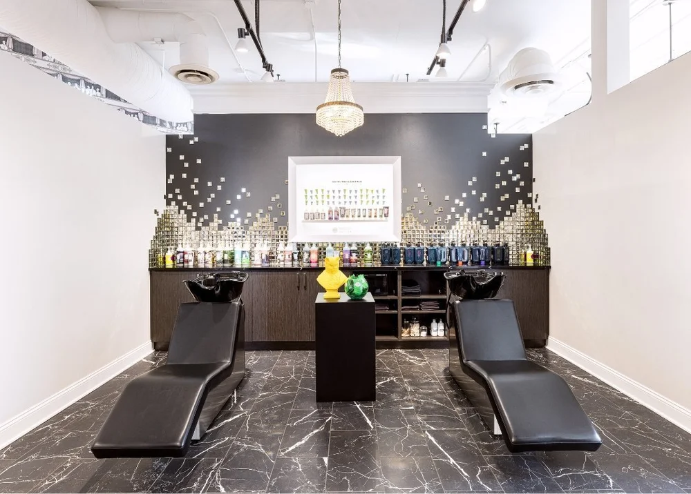 Two black shampoo chairs in the wash room under a crystal chandelier
