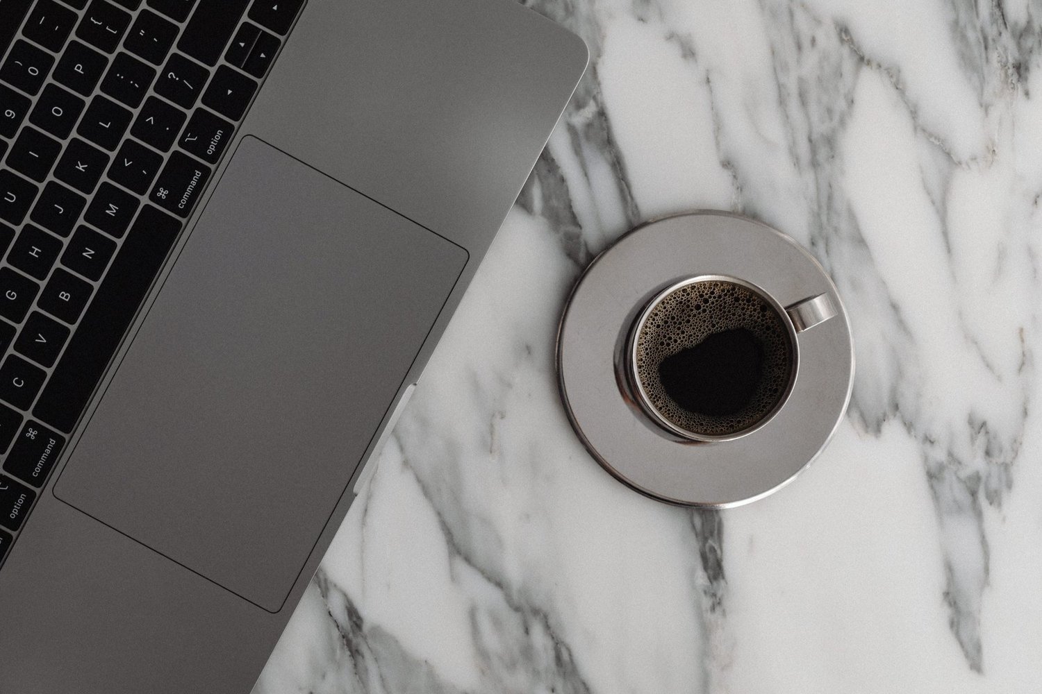 A laptop and a steel espresso cup on white marble
