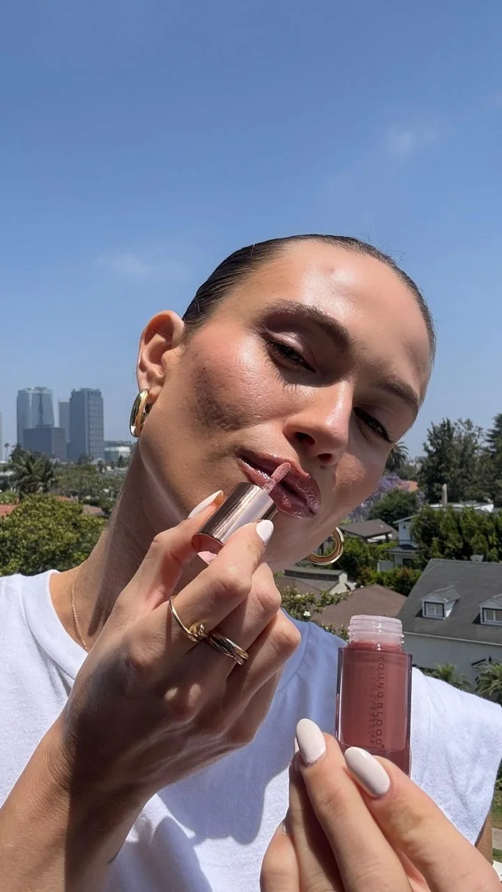 A creator applying EverGlow Lip Oil with a city skyline behind