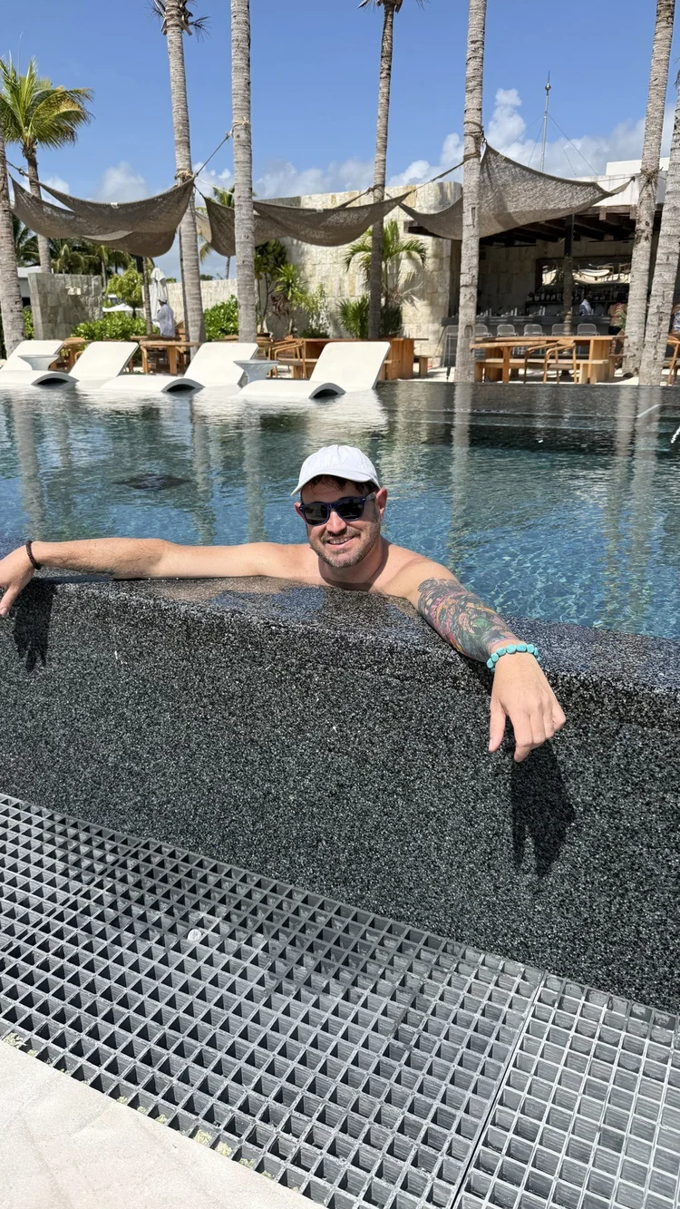 Sean Bryan relaxing in a resort infinity pool lined with palm trees