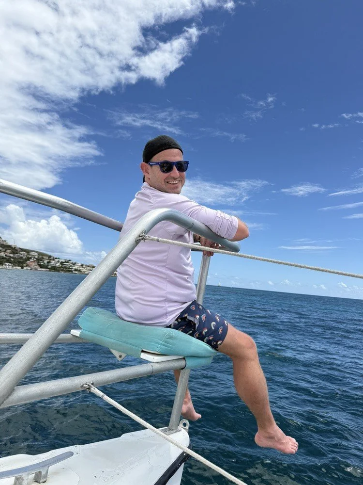 Sean Bryan sitting on the bow of a catamaran on a sunny Caribbean sail